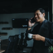 smiling man holding cup and using smartphone