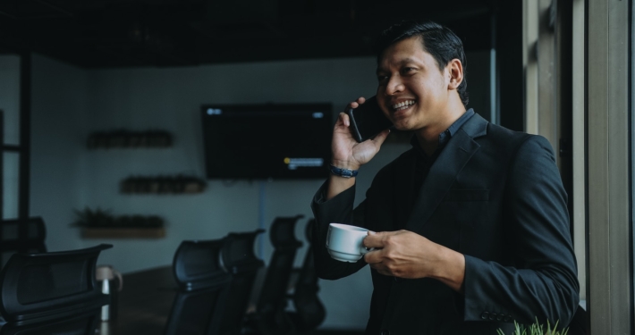 smiling man holding cup and using smartphone